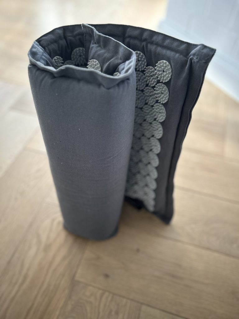 Eine eingerollte Akupressurmatte steht senkrecht auf einem Parkettboden. Diese Matten können überall mit hingenommen und flexibel verwendet werden.