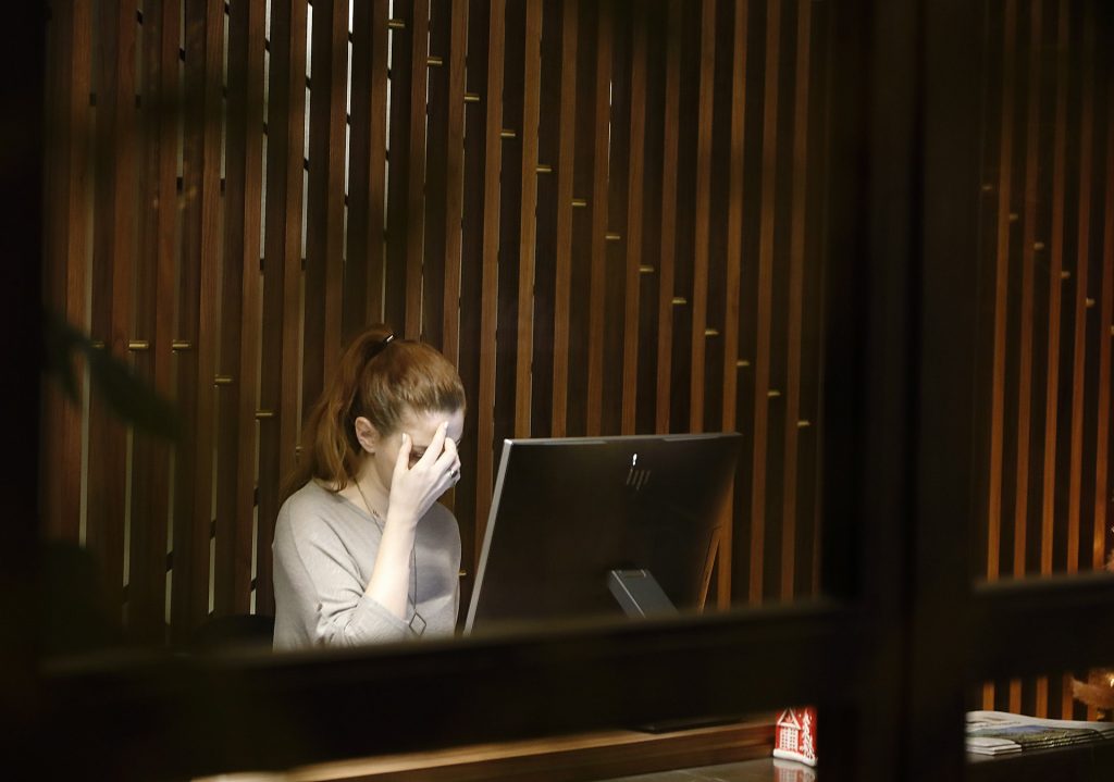 Eine Frau wird gezeigt, die am Computer arbeitet. Sie fasst sich mit einer Hand an den Kopf und es wirkt, als leide sie unter Kopfschmerzen.