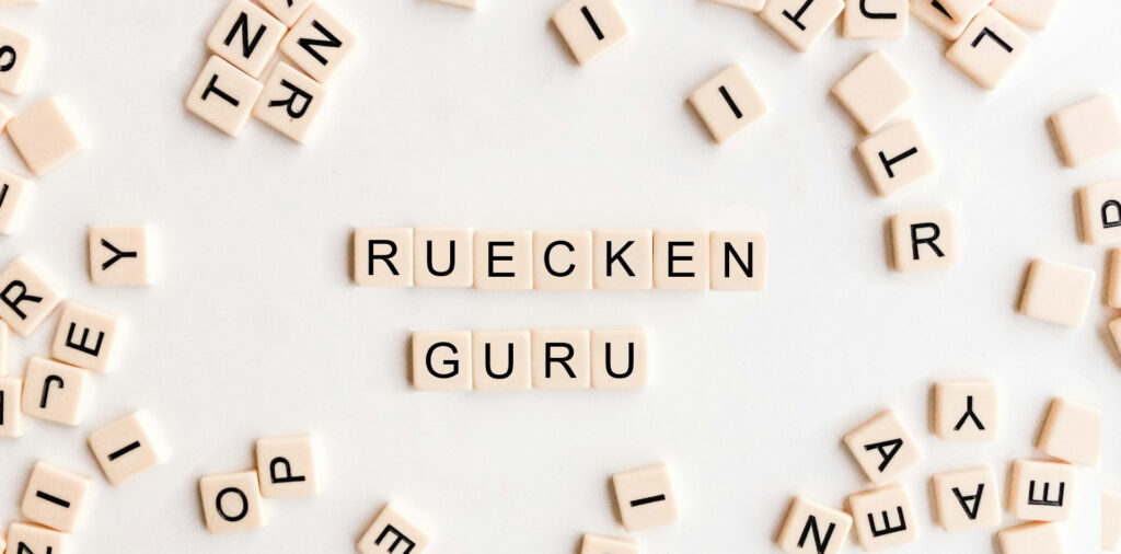 Einzelne Buchstabenplatten liegen auf einem Tisch, die Worte Ruecken und Guru sind mit den Platten zusammen angeordnet